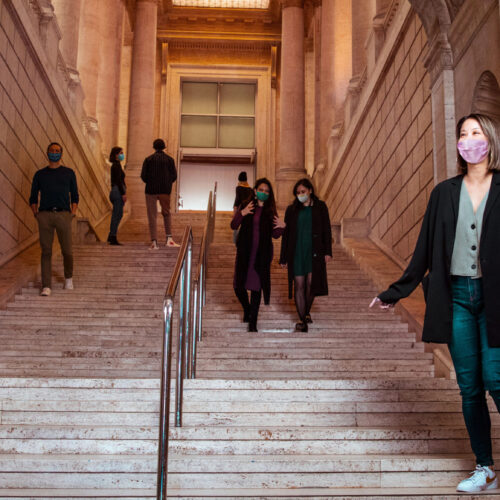 A woman wearing a mask descends a grand staircase.