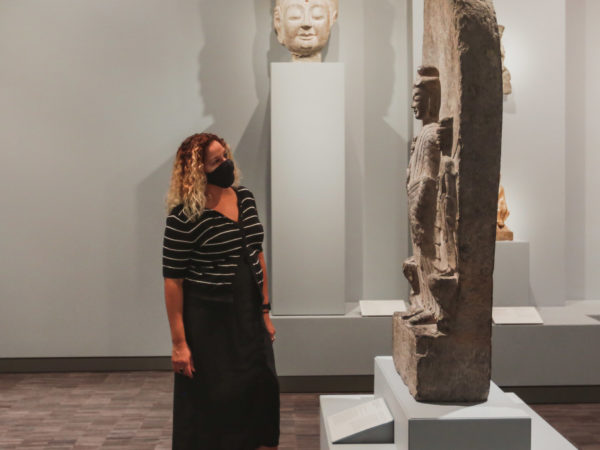 A woman wearing a mask looks at a stone statue.